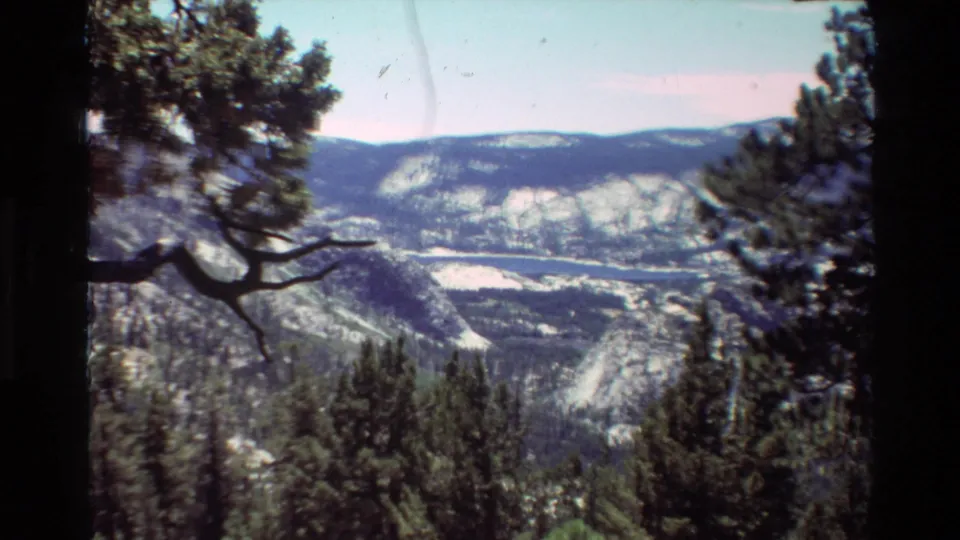 Scenic 8mm view from a wooded overlook toward a broad mountain valley and possible lake, following the family hiking shots in the clip.
