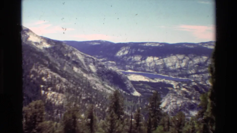 1981 8mm view across a British Columbia mountain range, showing a valley, distant lake or river, evergreens, and dark scan borders.