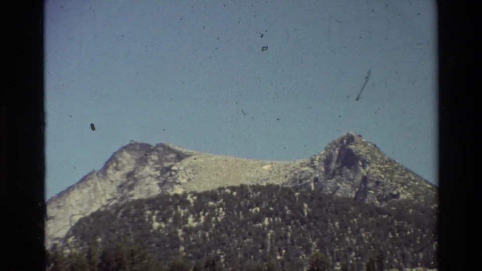 Cataloged 1981 8mm mountain vista with pale rocky peaks, dark tree-covered slopes, and visible film gate edges.