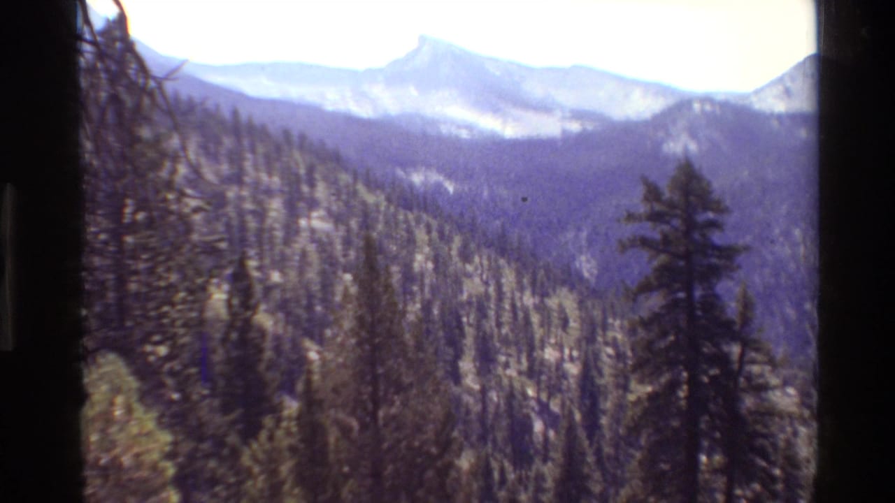 1981 8mm frame showing a distant mountain valley, forested ridges, and soft handheld exposure in a wilderness setting.