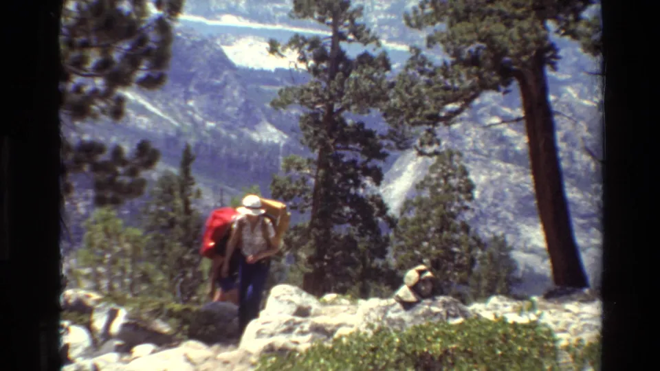 End frame of two hikers with heavy packs on a rocky mountain trail, filmed in the stated 1981 British Columbia home-movie clip.