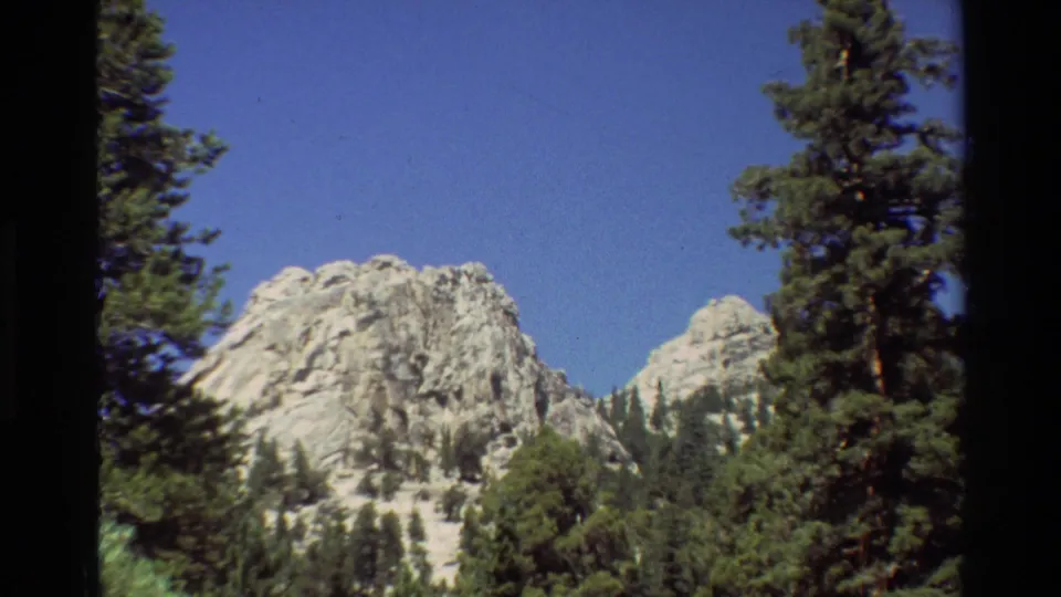 Metadata-listed 1981 travel footage shows a rocky peak framed by pines and visible 8mm gate edges.