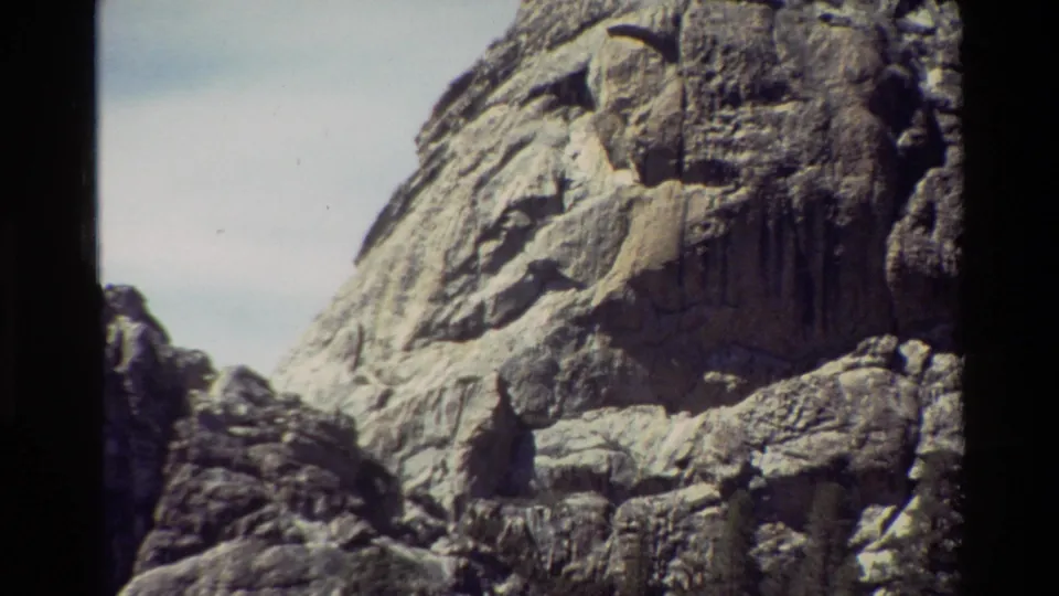 Archival 8mm frame of a rugged cliff face with layered granite texture and darker rocks in the foreground.