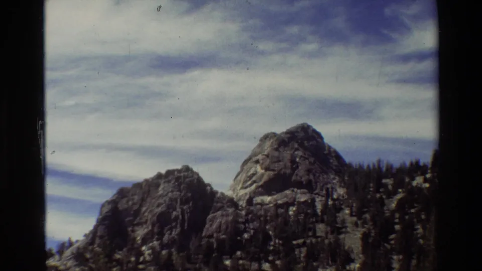 Final 1981 8mm frame of rugged peaks and evergreen forest, with soft color, grain, and contact-sheet borders visible.