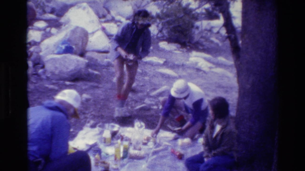 Four people in 1981 home-movie footage gather around a picnic blanket in a rocky outdoor setting, likely British Columbia.