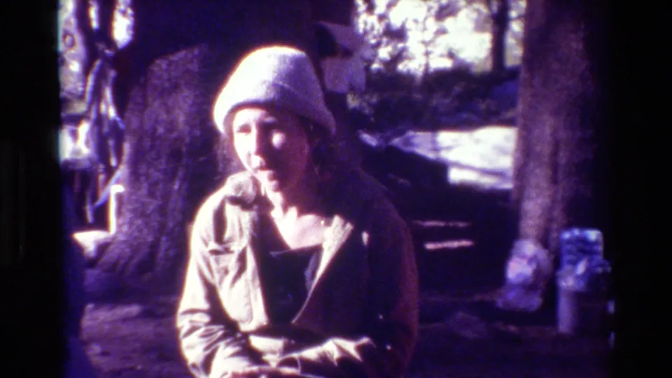 Metadata-supported 1981 8mm frame of a woman facing the camera in a wooded outdoor setting with a purple film cast.
