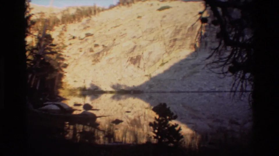 The final frame shows calm lake water mirroring a pale mountain slope, with trees and branches framing the view.