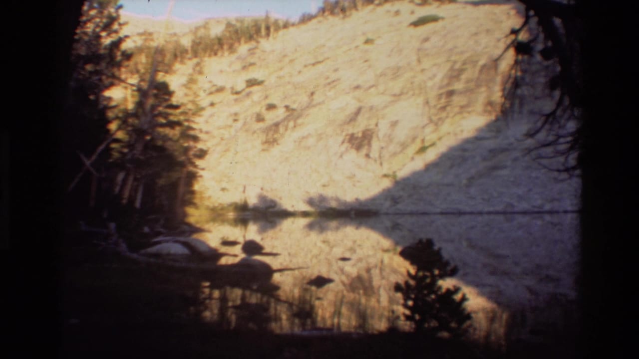 Still mountain lake reflecting a sunlit pale slope, framed by dark trees and shoreline silhouettes.