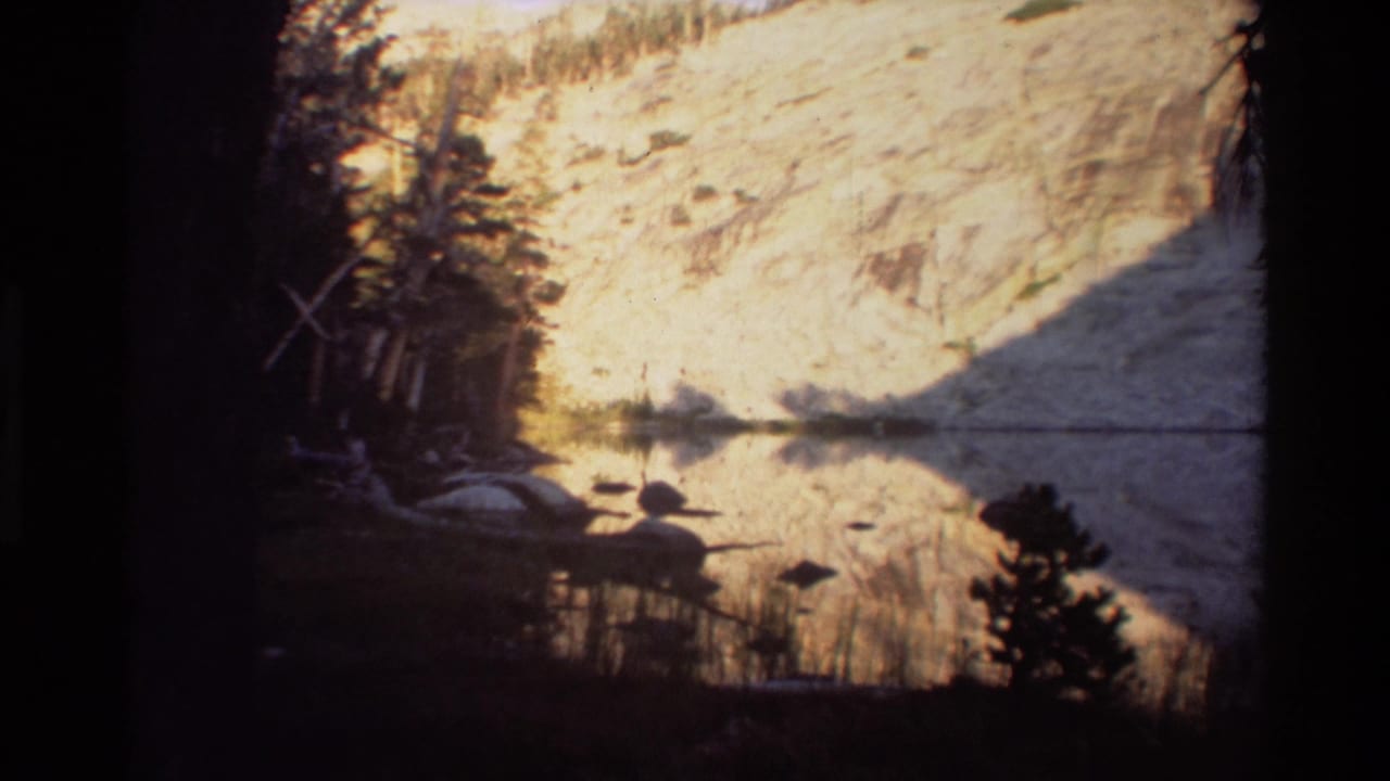 Mountain lake reflection with a pale hillside, dark tree line, and shadow across the water.