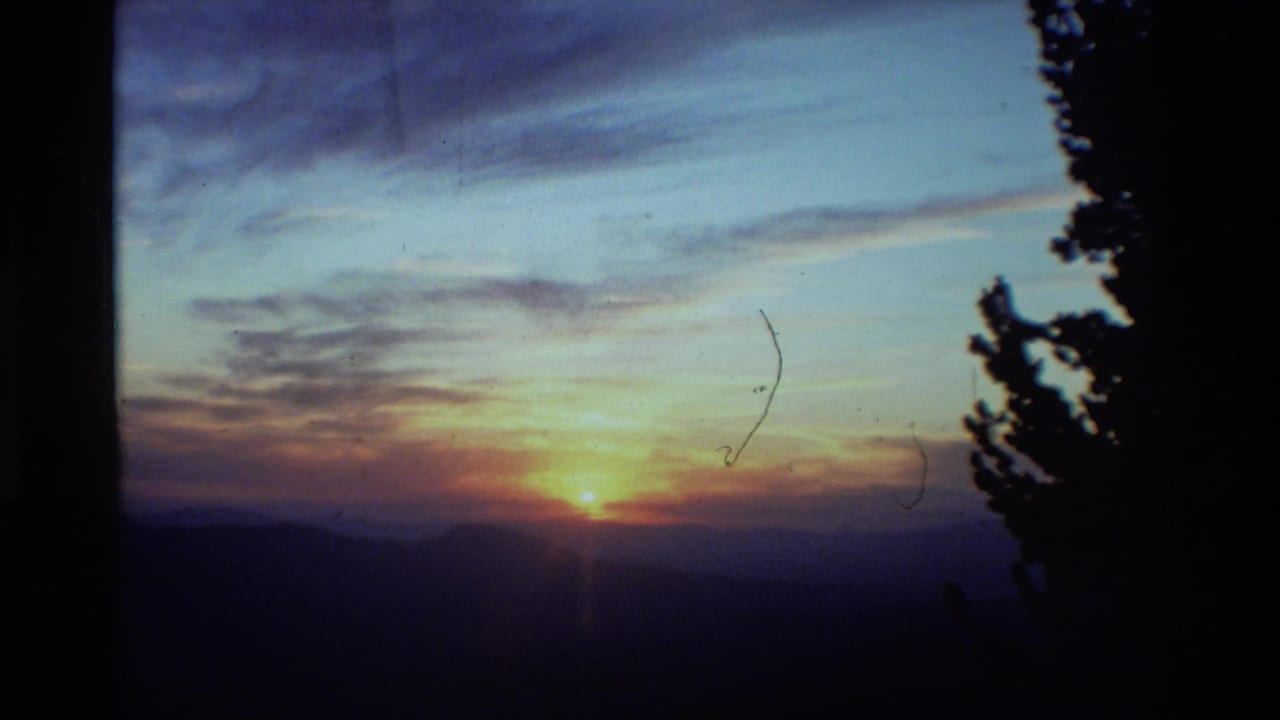 1981 8mm home-movie frame showing a small orange sun near the horizon over layered mountain silhouettes.
