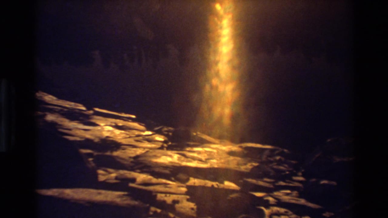 A vertical column of golden lens flare crosses rocky terrain, with the surrounding landscape mostly dark and softly exposed.