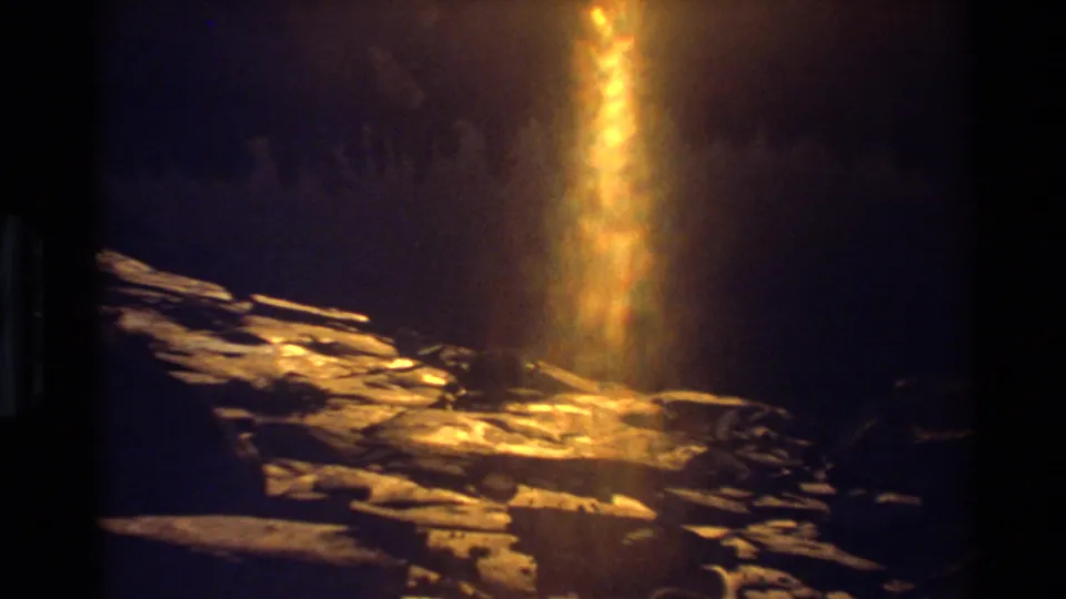 The 8mm frame emphasizes a bright vertical flare and reflected sunlight over layered rocks, with strong exposure bloom.
