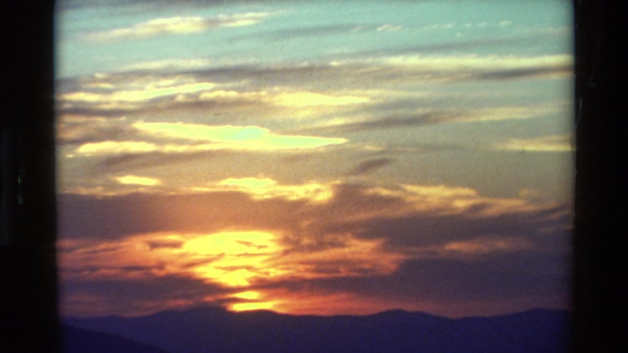 8mm sunset view with golden light breaking through clouds over distant mountain ridges.