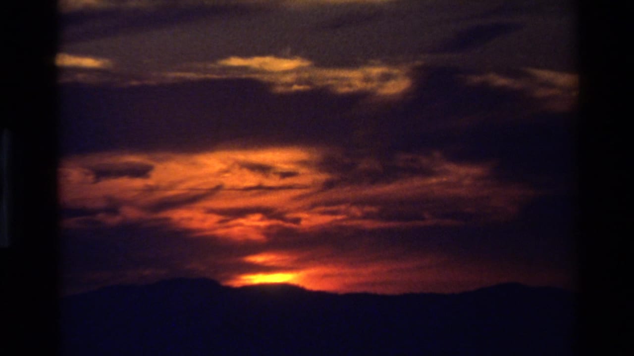 Warm sunset deepens over a dark ridgeline, with orange cloud bands and visible 8mm home-movie softness.