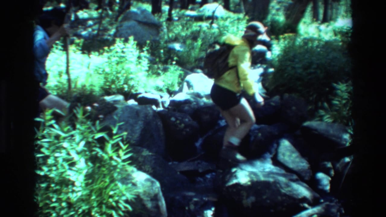 Listed British Columbia 1981 home-movie frame showing a hiker carefully crossing rocks in a shaded forest stream.