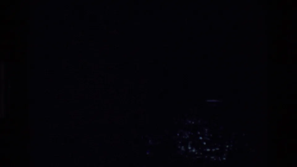 Dark opening 8mm frame with only faint blue highlights suggesting the river and trees visible in later frames.