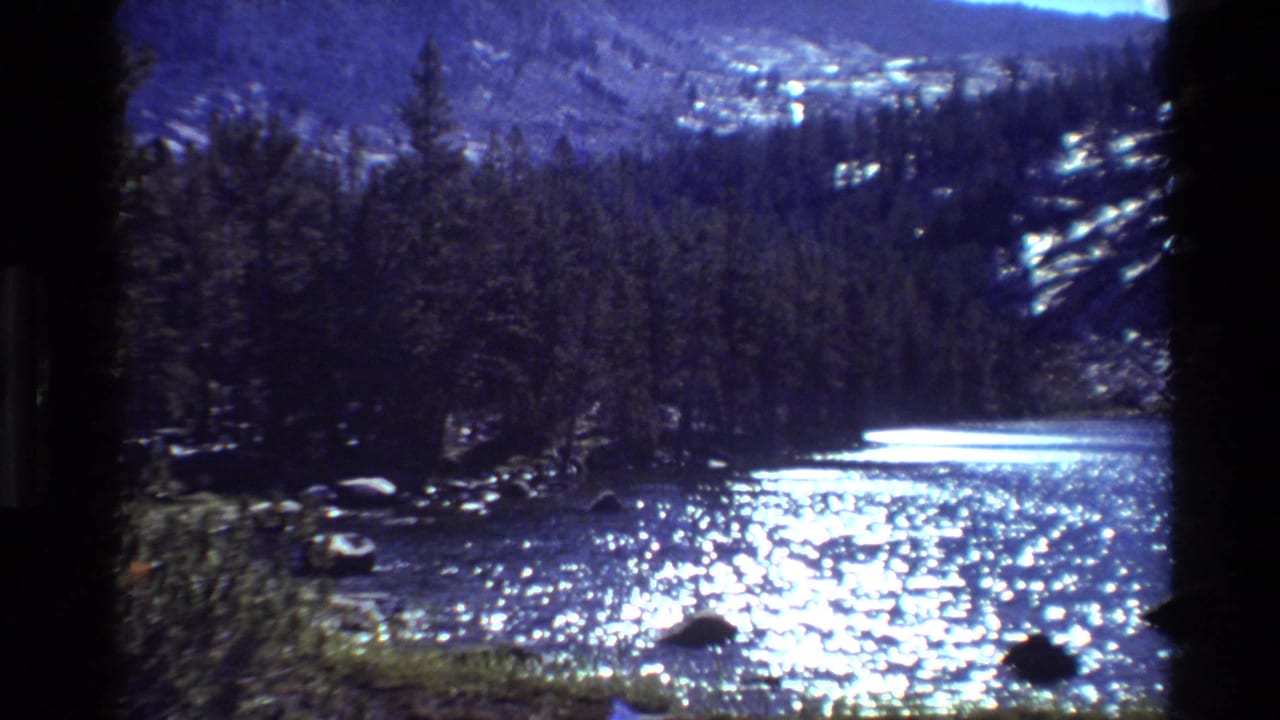 Metadata-supported 1981 8mm view of a bright river in British Columbia, with evergreen trees, rocks, and distant slopes.