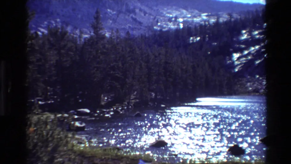 Metadata-supported 1981 8mm view of a bright river in British Columbia, with evergreen trees, rocks, and distant slopes.