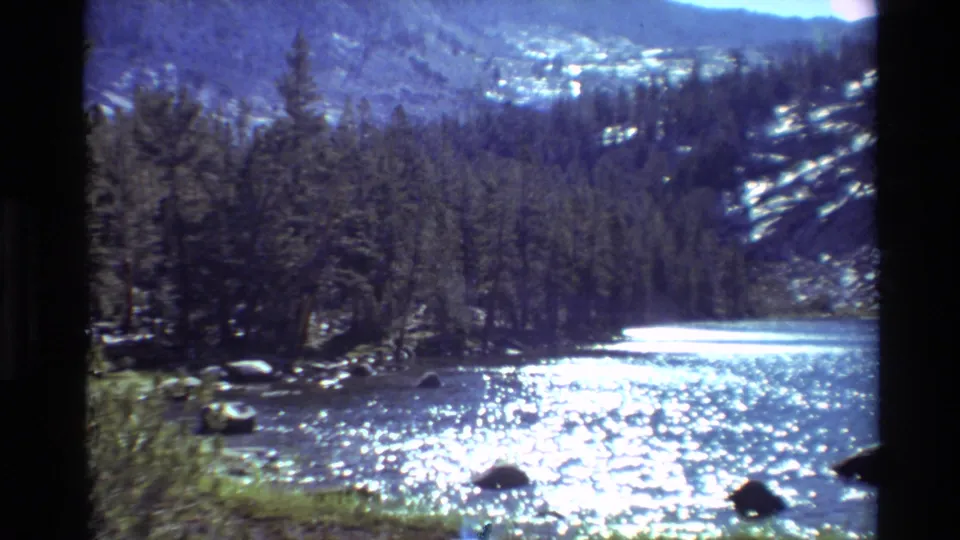 1981 8mm home-movie frame showing a forested mountain river with strong sunlight glittering on the water.