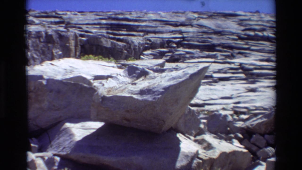 Layered rock ledges and a large sunlit boulder under a blue sky.