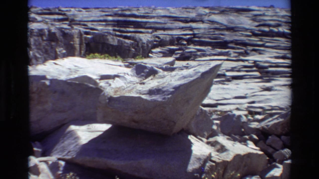Metadata-labeled 1981 British Columbia/USA home-movie view of a large boulder against horizontal rock strata and blue sky.