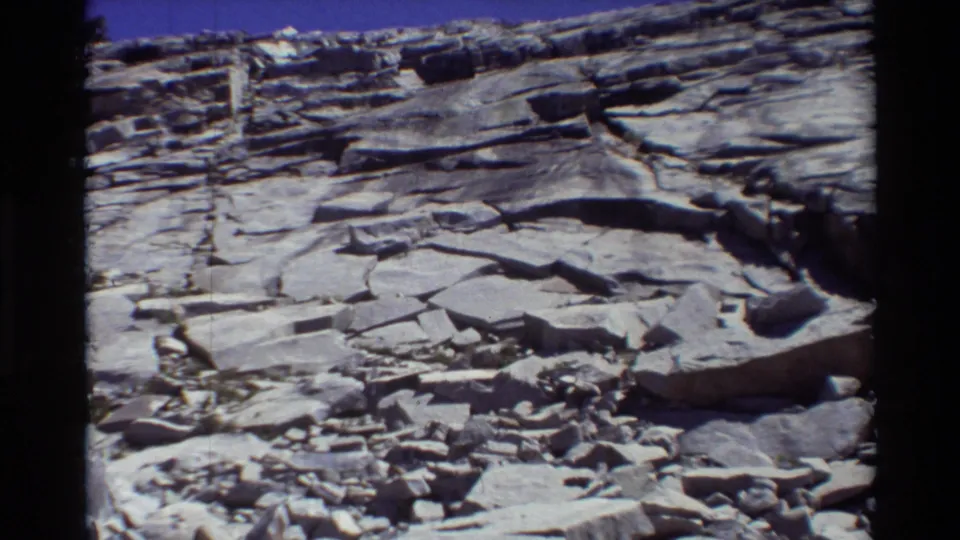 1981 8mm frame showing cracked stone slabs, loose rocks, and layered terrain in a rugged outdoor landscape.