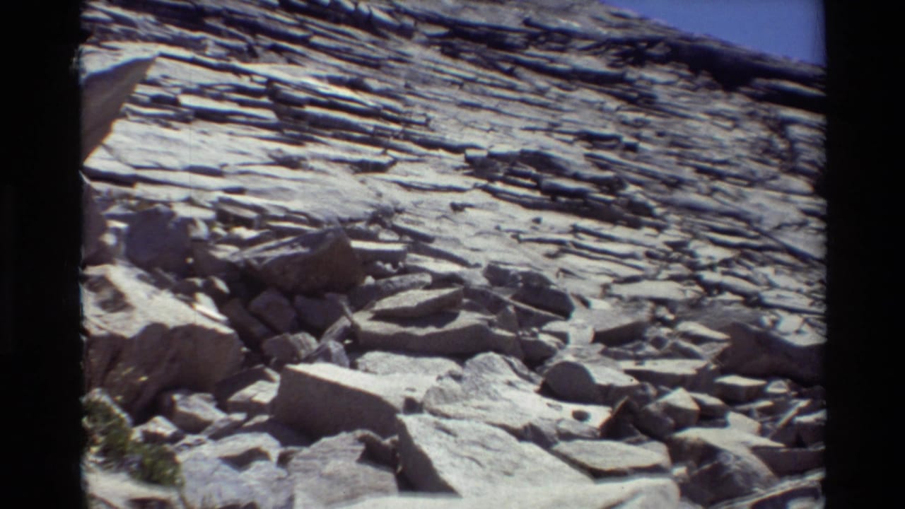 Rocky slope with large boulders below a stratified stone wall.