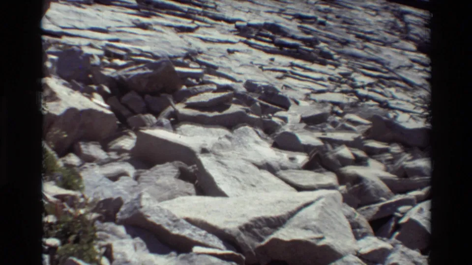 1981 8mm frame cataloged to British Columbia showing pale angular boulders in the foreground with horizontal rock layers behind them.