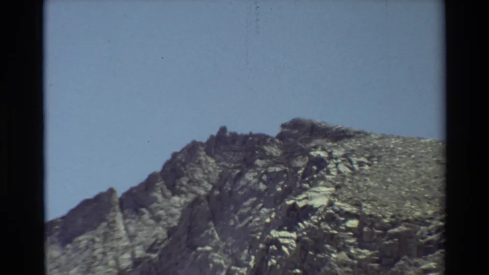 1981 8mm home-movie frame showing a closer craggy mountain ridge, with rough gray rock textures and open sky.