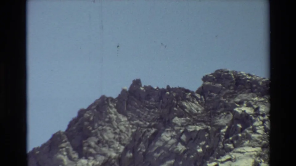 1981 8mm home-movie frame with a close view of rugged summit rocks and shadowed stone under a pale blue sky.