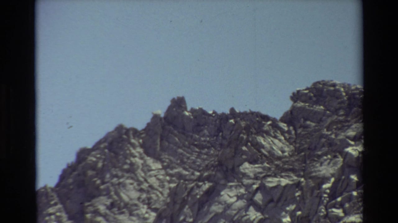 Rocky mountain ridge framed by dark film edges beneath blue sky.