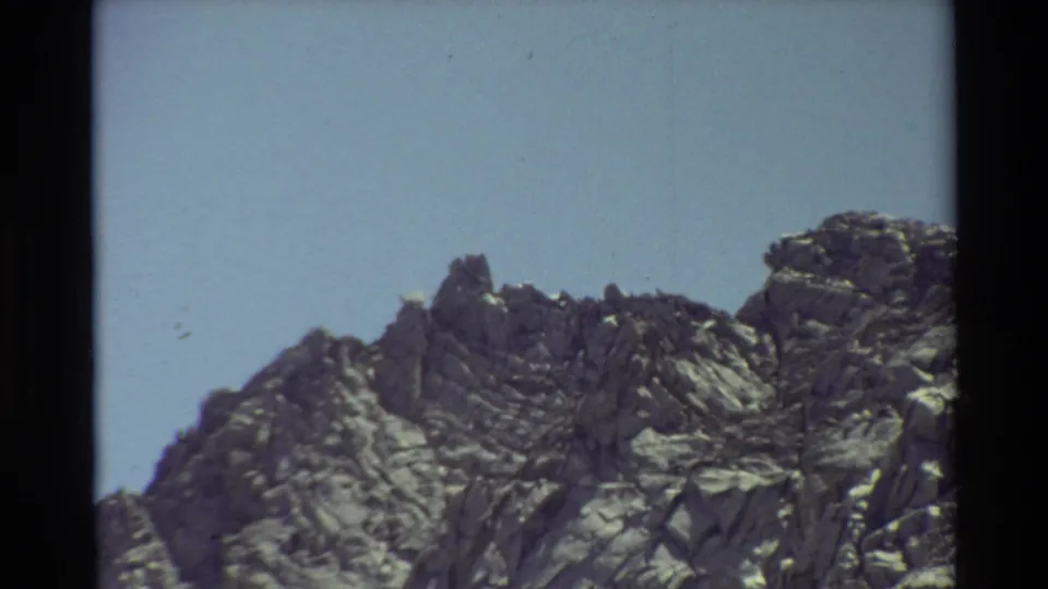Jagged alpine rocks fill the frame, with blue sky and visible 8mm film borders from the 1981 home movie.
