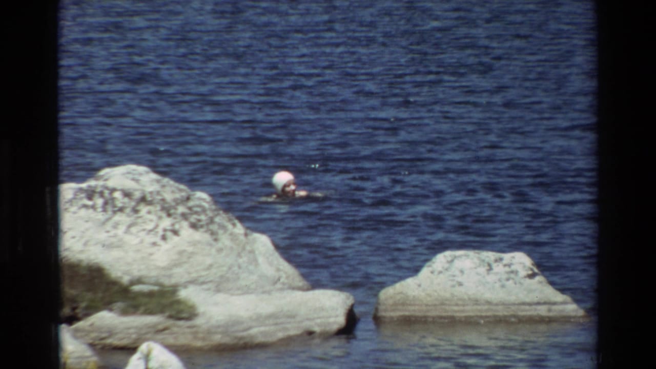 Woman swimming behind a large pale rock in blue water.