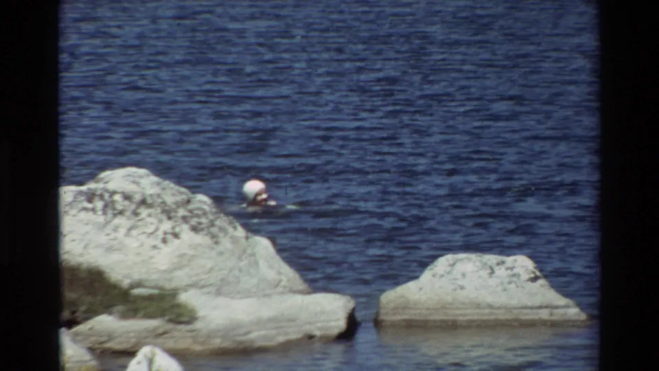 A steady 8mm frame shows the swimmer moving beside large pale rocks, with blue water filling most of the view.