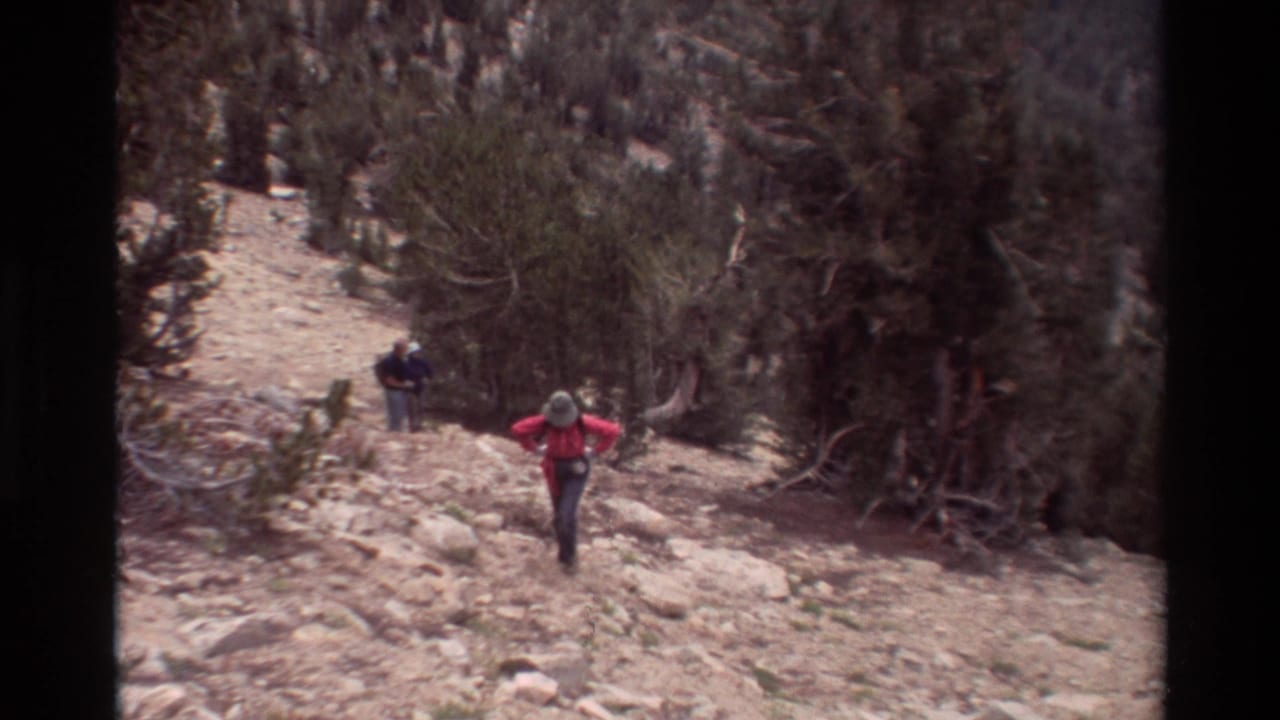 Hiker in a red jacket climbing a rocky mountain trail with another hiker behind.