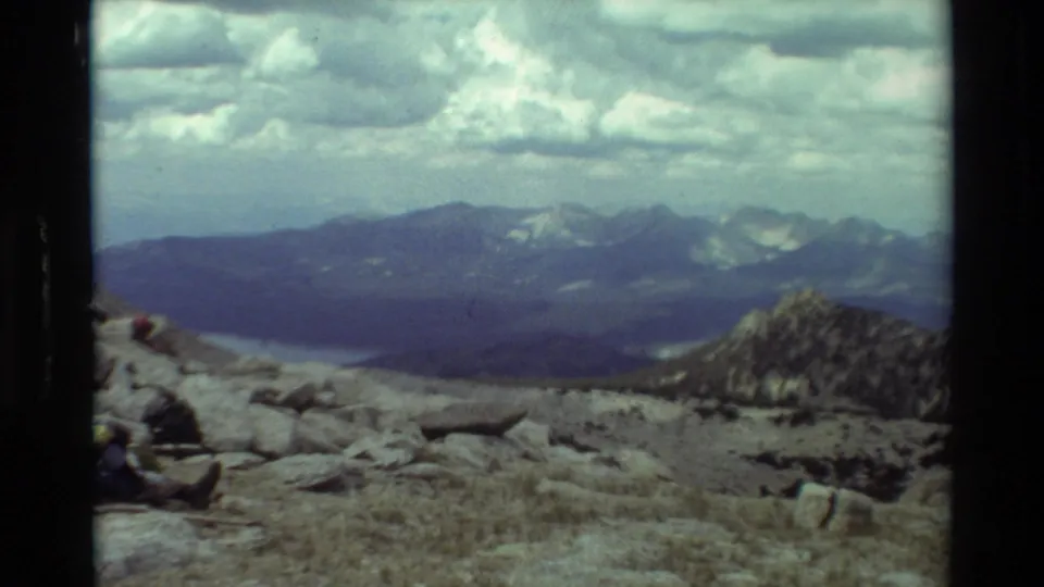 Wide 8mm view across a rocky British Columbia alpine overlook toward a valley, lake, distant peaks, and layered clouds.