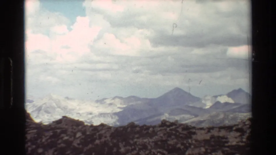 Supported 1981 8mm frame showing a rocky alpine ridge and distant snow-patched peaks under a cloudy sky.