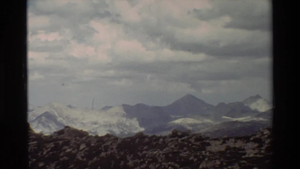 Supported 1981 8mm frame showing a wide mountain vista with dark peaks, broken clouds, and rocky alpine ground.