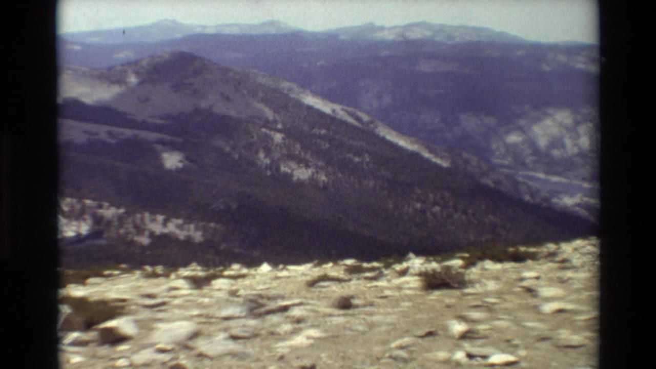Cataloged 1981 8mm footage shows a rocky mountain overlook with distant ridges, valley slopes, and sparse scrub in the foreground.