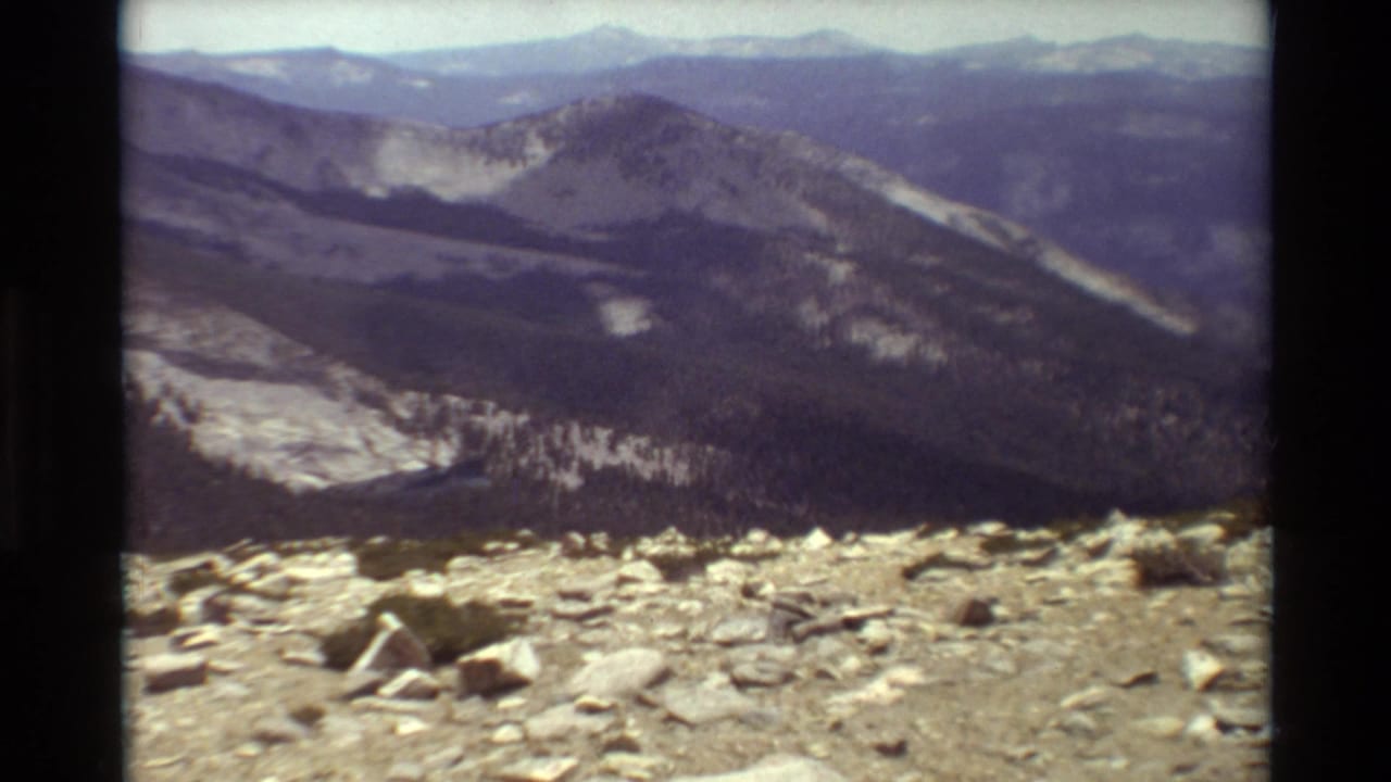The frame continues the cataloged mountain view, with loose stones in front and layered ridges receding through haze.