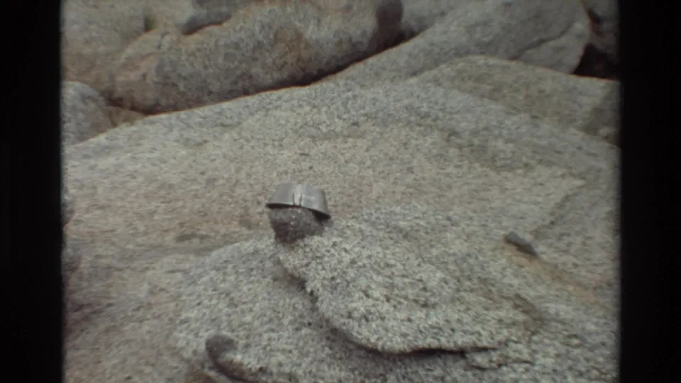 The final frame shifts to a close view of a small metal object on a gray rock surface, with larger boulders behind it.