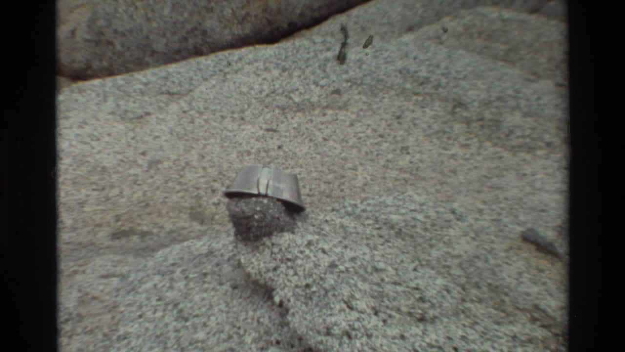 Close-up 8mm frame from the 1981 British Columbia metadata showing a small metal pot or cup on rough gray stone.