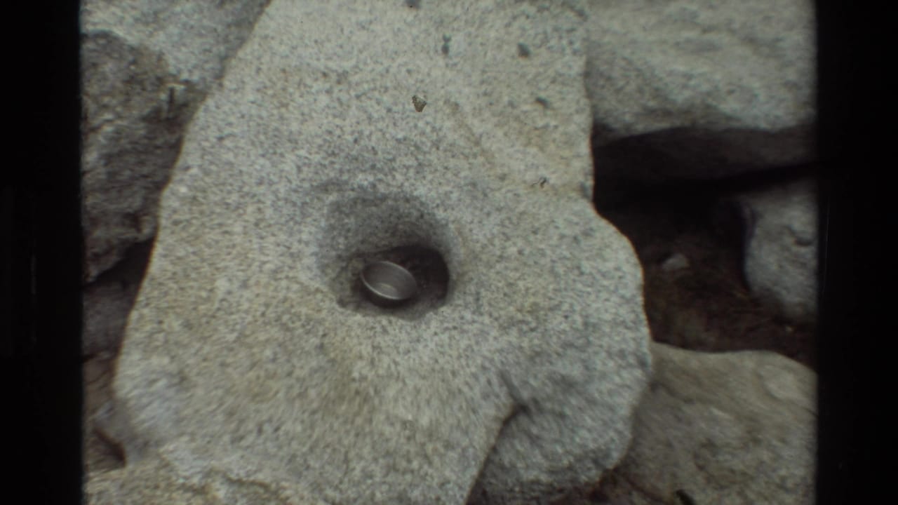 The small metal pot or cup appears nestled inside a shallow hand-shaped hollow in a large gray rock.