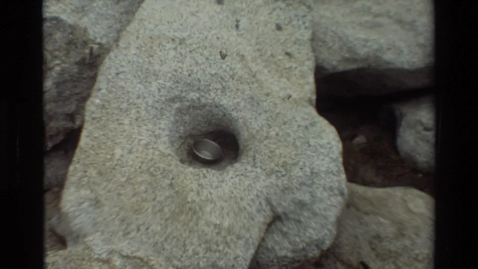 The small metal pot or cup appears nestled inside a shallow hand-shaped hollow in a large gray rock.