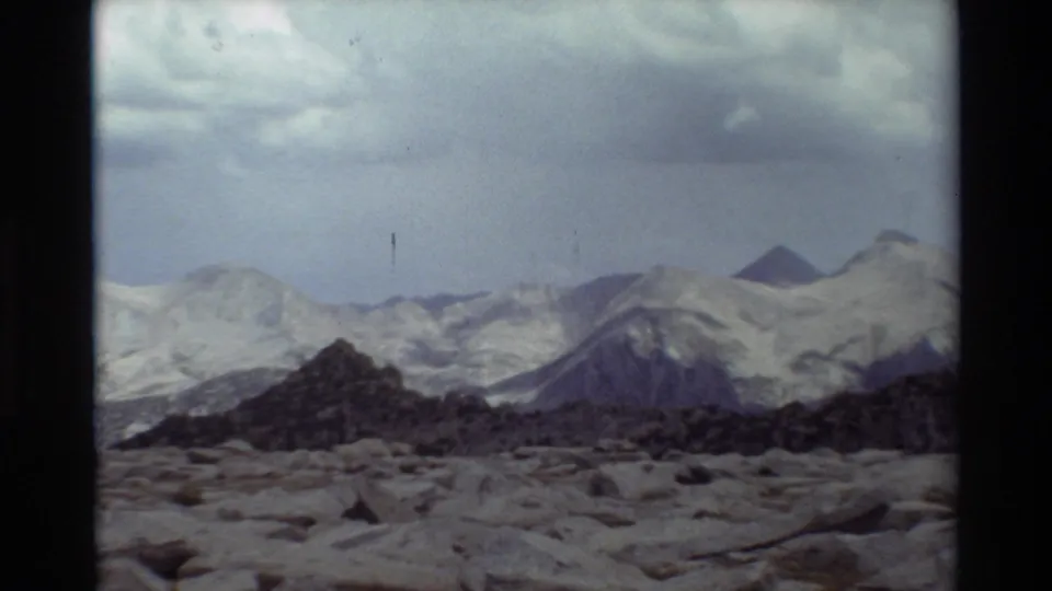 Final 8mm frame of the mountain range, with rocky terrain, dark ridgeline, pale peaks, and visible film wear.