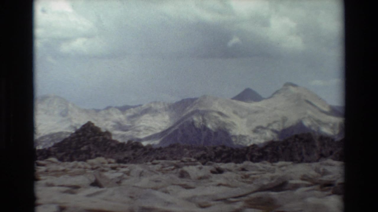 1981 8mm frame of distant snow-covered mountain peaks and rocky foreground terrain, described by metadata as British Columbia.