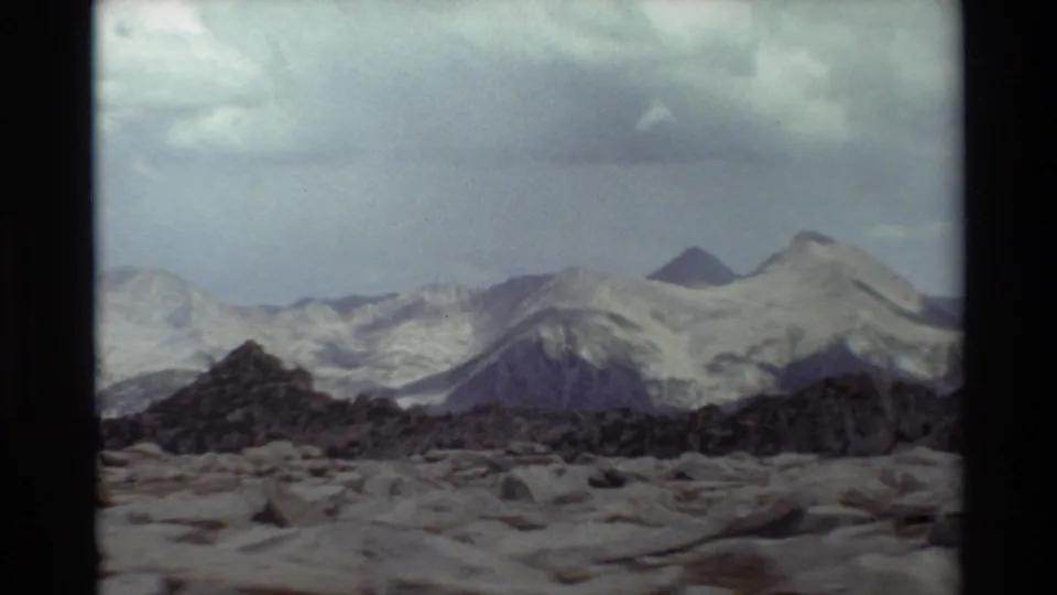 1981 8mm frame of distant snow-covered mountain peaks and rocky foreground terrain, described by metadata as British Columbia.
