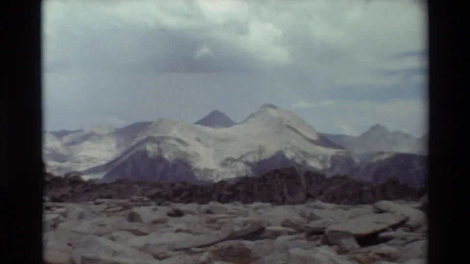 Vintage 8mm view of a rocky overlook facing layered alpine ridges and snow-streaked peaks, with location supported by clip metadata.