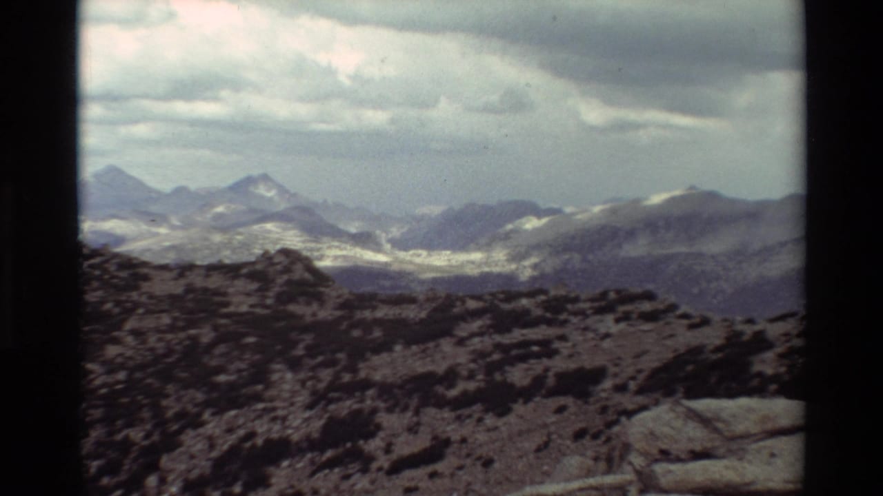 Rocky mountain overlook with distant snow patches and cloudy sky.