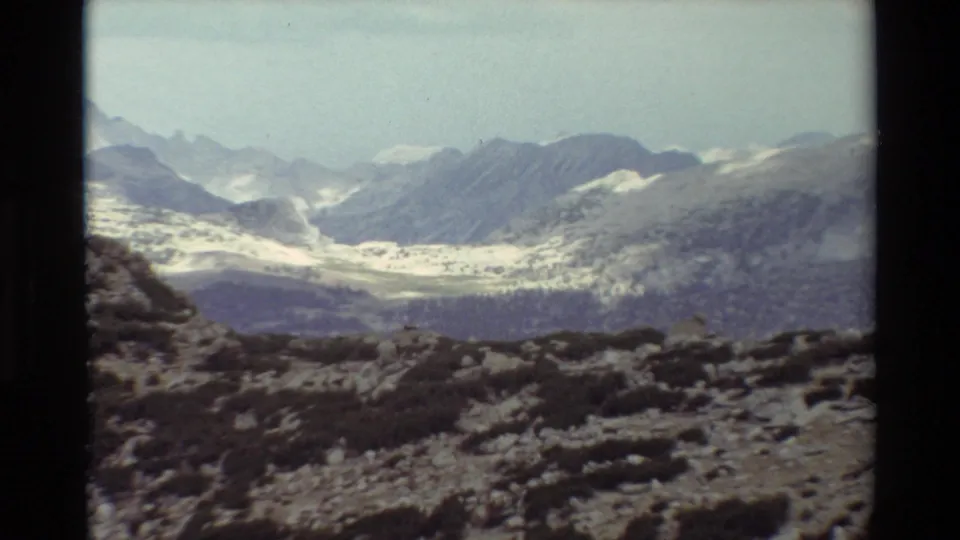 1981 8mm landscape frame looking over rocks and low brush toward layered mountains and scattered snow in British Columbia metadata context.